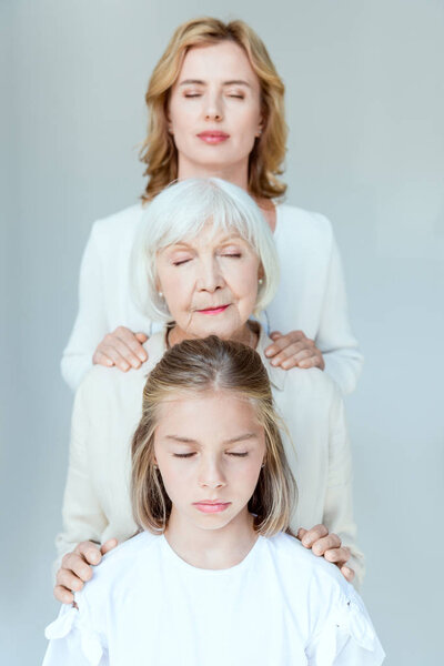 granddaughter, grandmother and mother with closed eyes hugging isolated on grey 