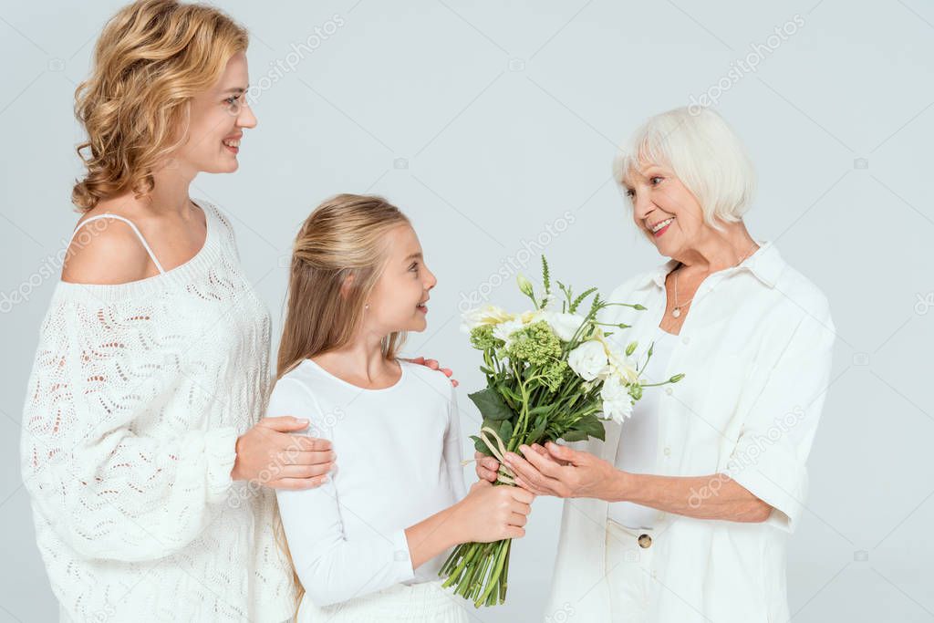 smiling granddaughter giving bouquet to grandmother isolated on grey 