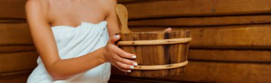 panoramic shot of woman holding wooden washtub in sauna  clipart