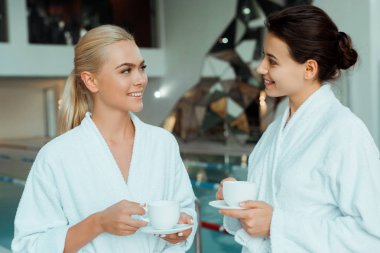 Beyaz bornozlu gülümseyen arkadaşlar kaplıcada konuşup bardaklar tutuyorlar. 