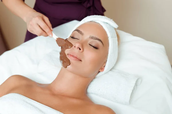 Kozmetik uzmanının kaplıcadaki çekici kadına yüz maskesi takması. 