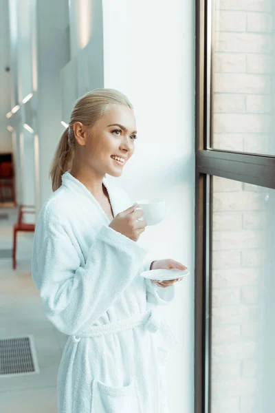 Mulher Atraente Sorridente Roupão Branco Segurando Xícara Café Olhando Através — Fotografia de Stock