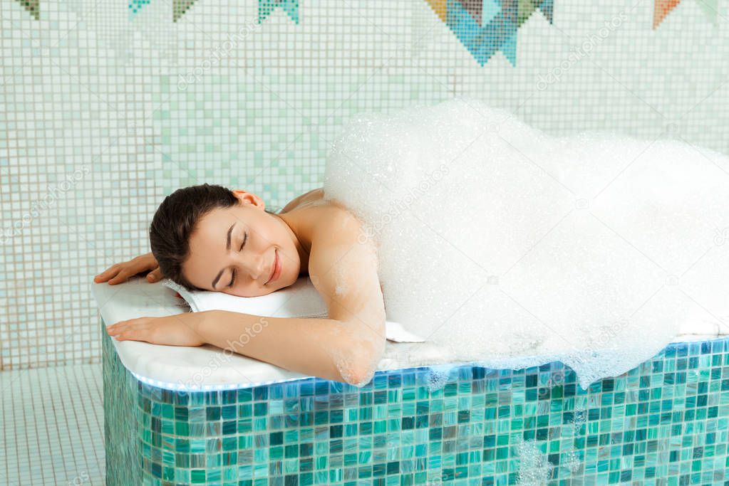 attractive woman lying on hammam table with foam in turkish bath