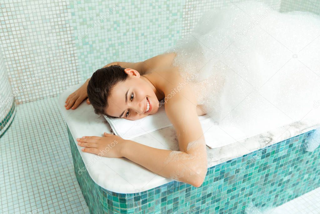 high angle view of smiling woman lying on hammam table with foam in turkish bath