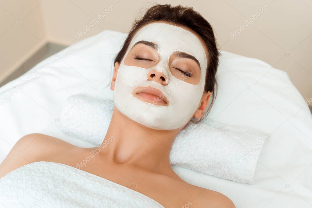 high angle view of attractive woman with mask on face lying on massage table in spa 