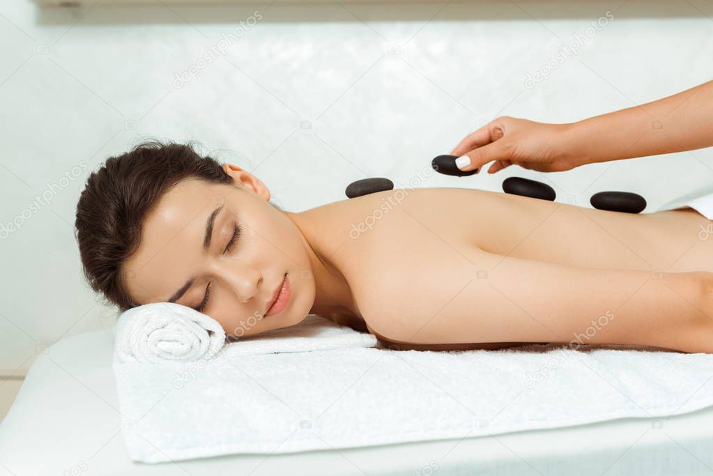 cropped view of masseur doing hot stone massage to attractive woman in spa 