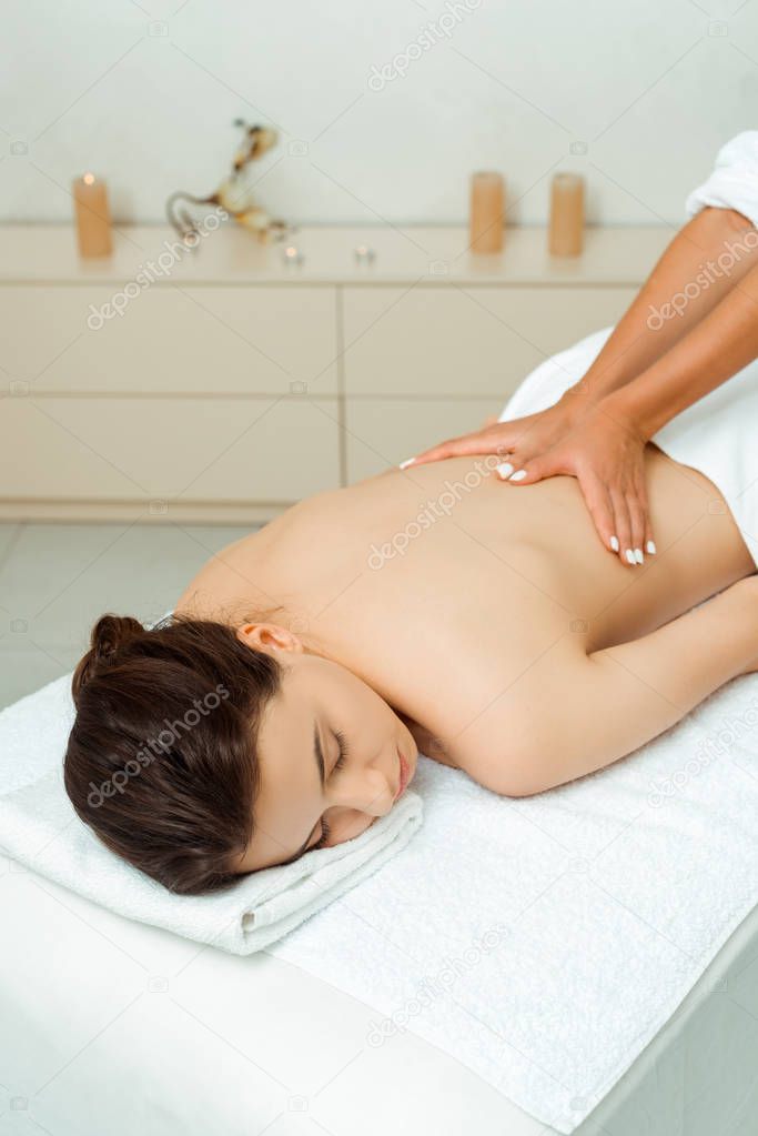 cropped view of masseur doing back massage to attractive woman in spa 