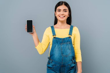 Gülümseyen hamile güzel kız gri ekranda boş ekranlı akıllı telefonu tutuyor.