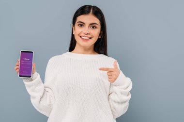 Kyiv, Ukrayna - 20 Eylül 2019: gri renkli Instagram uygulamalı akıllı telefonu işaret eden beyaz kazaklı güzel esmer kız