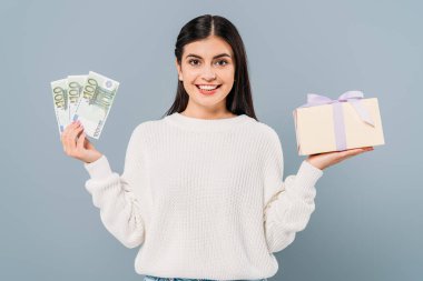 Gülümseyen, beyaz kazaklı, elinde euro banknotları ve gri renkli hediye kutusu tutan güzel bir kız.
