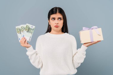 sad pretty girl in white sweater holding euro banknotes and gift box isolated on grey clipart