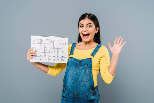 excited pregnant pretty girl holding period calendar isolated on grey