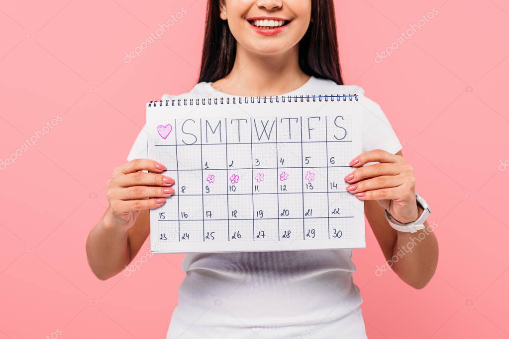 cropped view of smiling girl holding period calendar isolated on pink