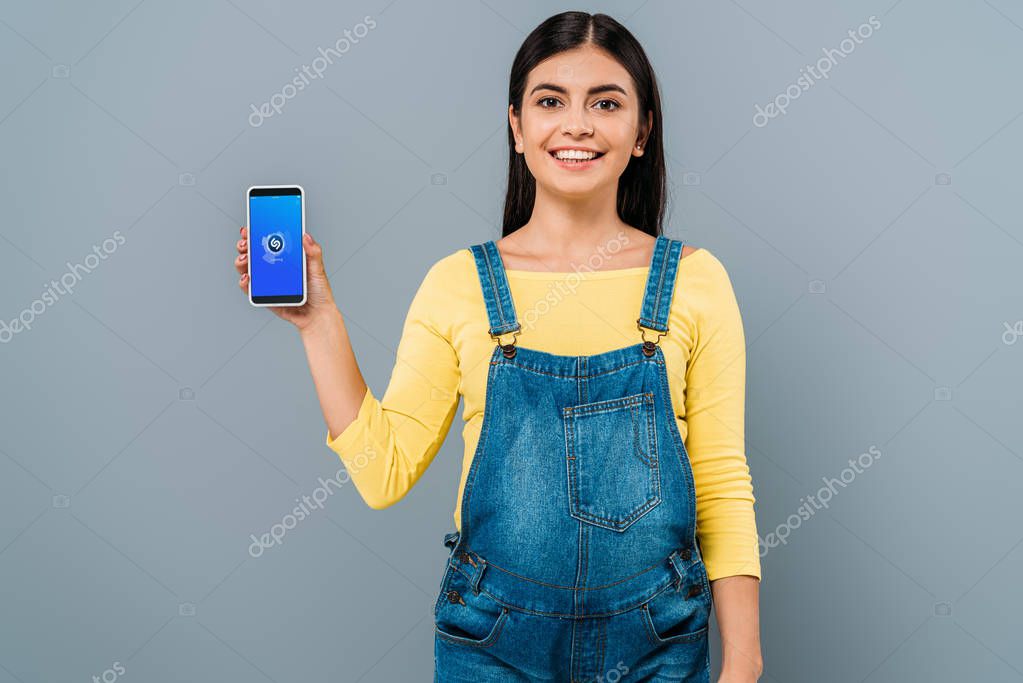 KYIV, UKRAINE - SEPTEMBER 20, 2019: smiling pregnant pretty girl holding smartphone with shazam app isolated on grey