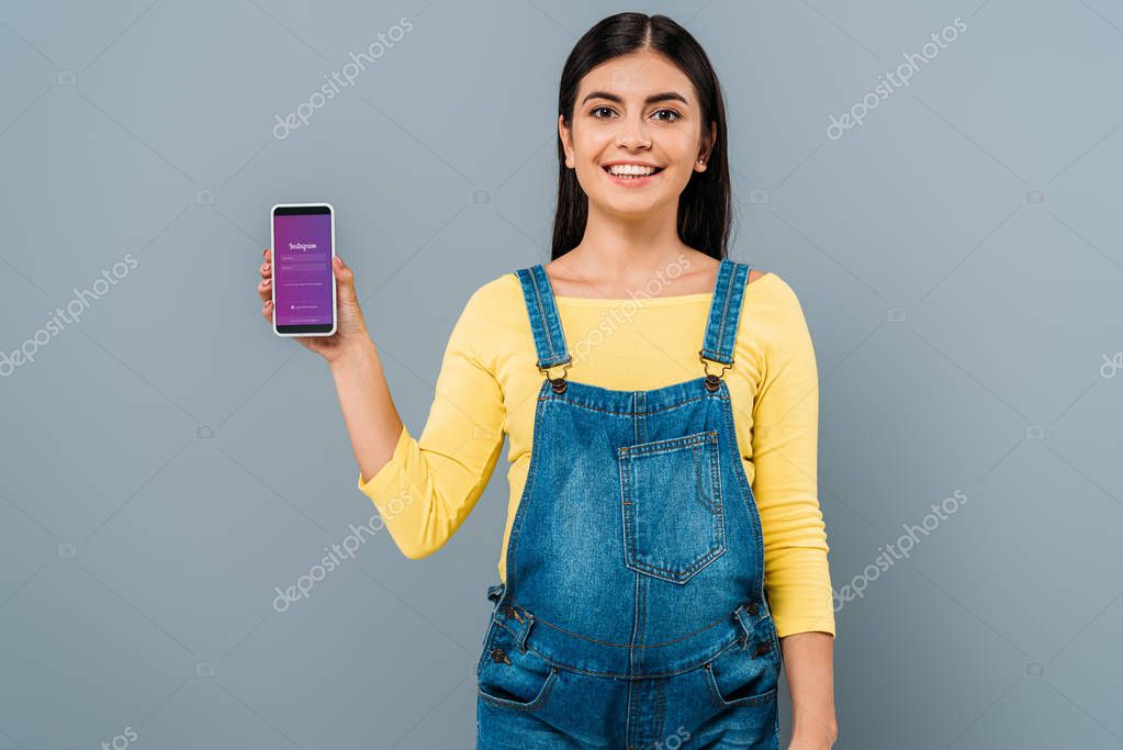 KYIV, UKRAINE - SEPTEMBER 20, 2019: smiling pregnant pretty girl holding smartphone with Instagram app isolated on grey