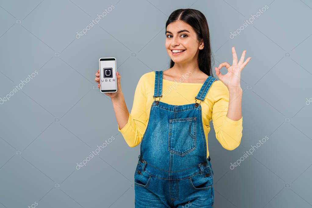 KYIV, UKRAINE - SEPTEMBER 20, 2019: smiling pregnant pretty girl holding smartphone with uber app isolated on grey