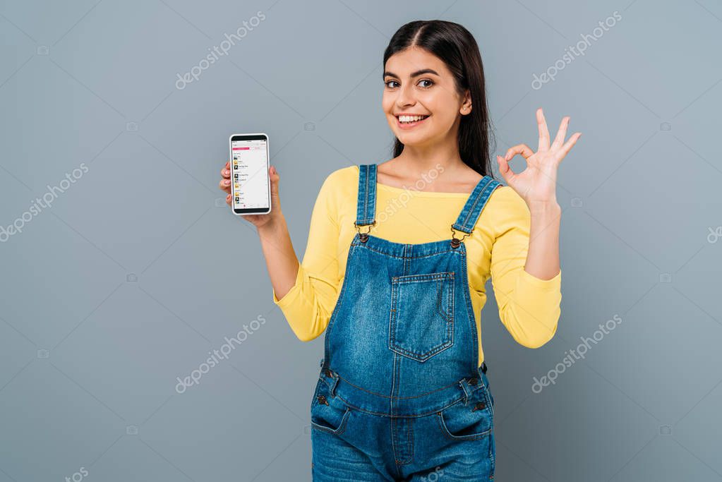 KYIV, UKRAINE - SEPTEMBER 20, 2019: smiling pregnant pretty girl holding smartphone with apple music app isolated on grey