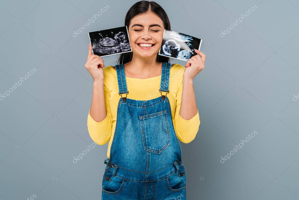 Happy pregnant pretty girl holding fetal ultrasound images isolated on grey