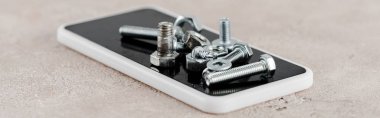 Gri arkaplanda akıllı telefondaki metal vidalar ve cıvatalar, panoramik çekim