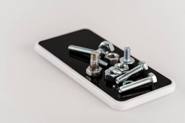 Beyaz arka planda akıllı telefondaki metal vidalar ve cıvatalar