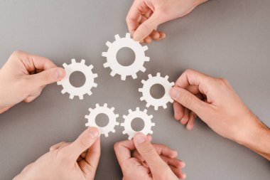 cropped view of people holding white gears on grey background clipart