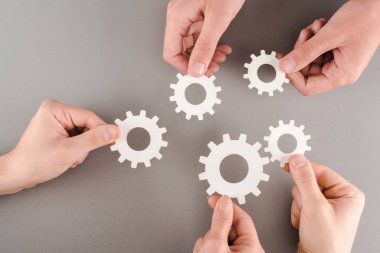 cropped view of people holding white gears on grey background clipart