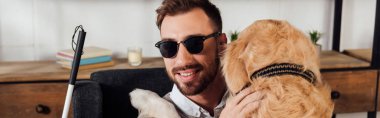 Gülümseyen kör adam evde Golden Retriever 'a sarılıyor, panoramik çekim