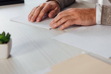 Cropped view of blind man reading braille font from paper at table clipart