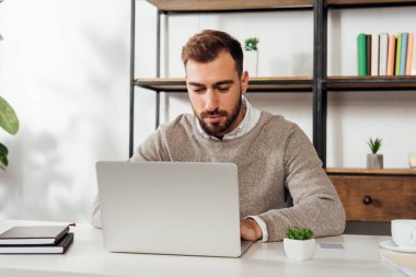 Masada çalışırken laptop kullanan yakışıklı adam. 