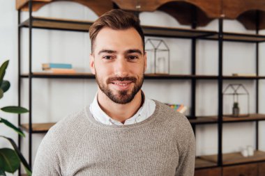 Evde kameraya gülümseyen yakışıklı bir adam.