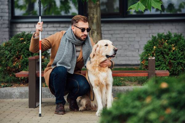 Blind man with walking stick hugging guide dog on street 