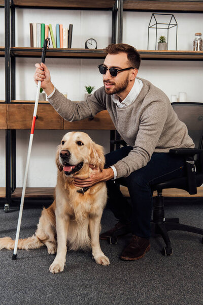 Blind man with walking stick petting golden retriever at home