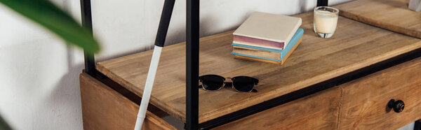 Panoramic shot of walking stick beside sunglasses and books on cupboard shelf