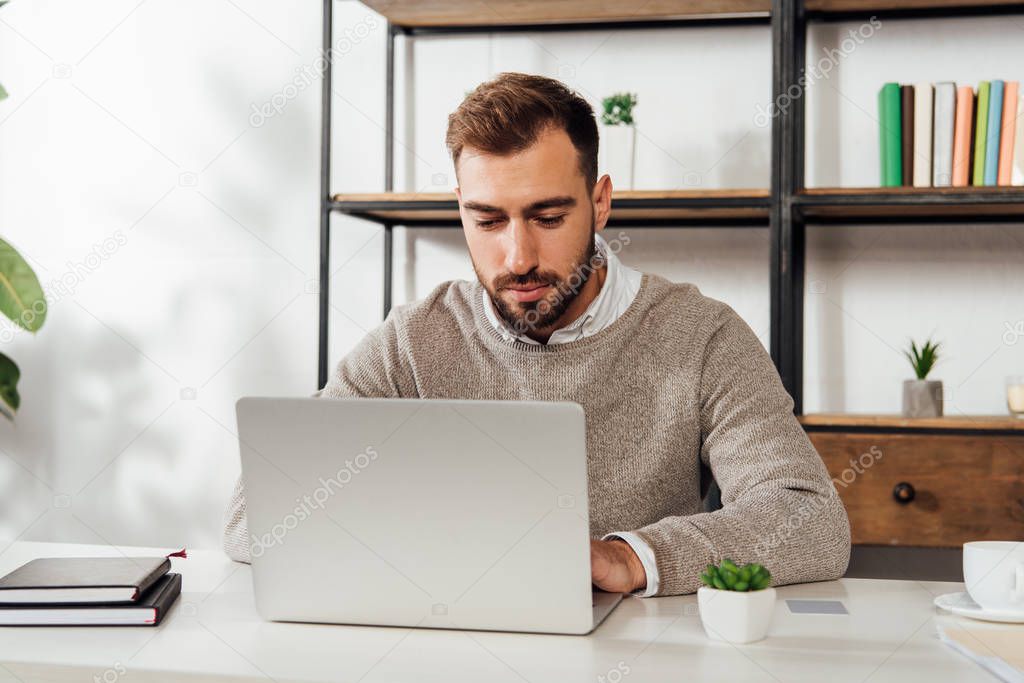 Handsome man using laptop while working at table 