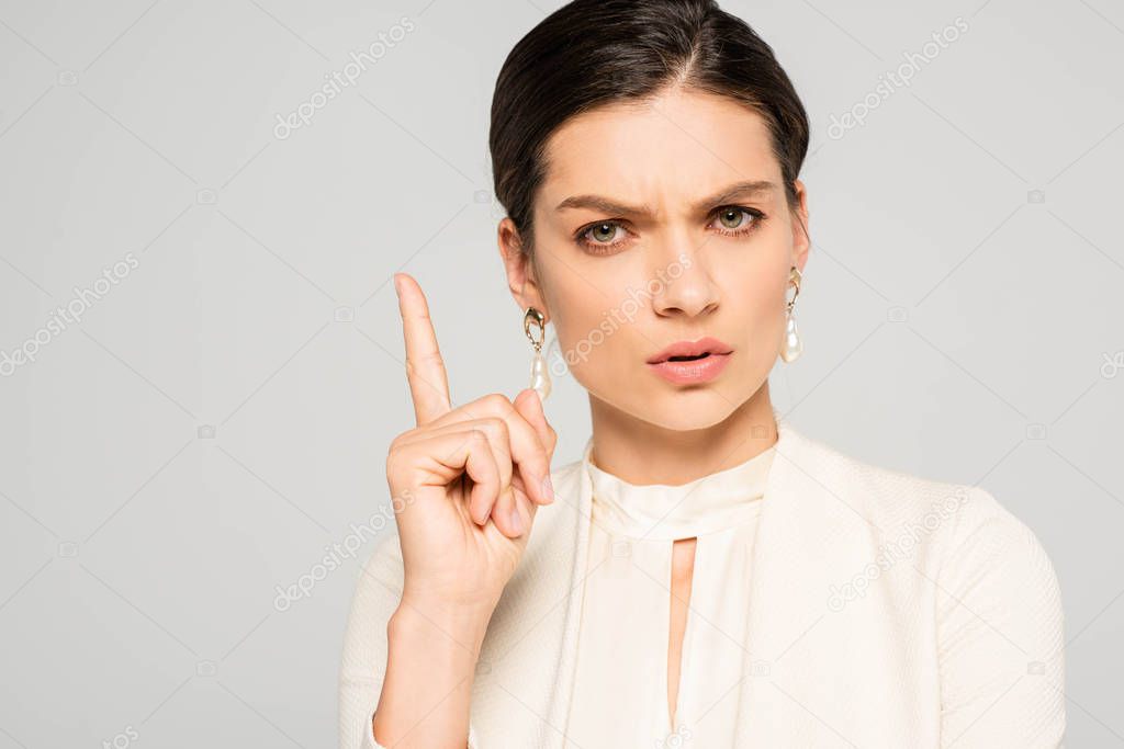worried businesswoman in white suit pointing up, isolated on grey