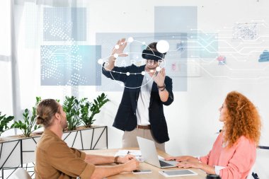 smiling businessman with vr headset gesturing in office near colleagues and startup illustration clipart