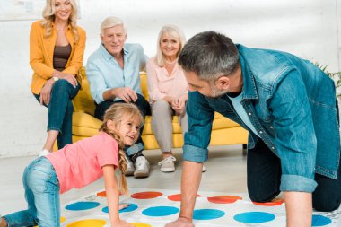 Kyiv, Ukrayna - 21 Kasım 2019: neşeli baba-kız kanepeye oturmuş ailenin yanında twister oyunu oynuyorlar.