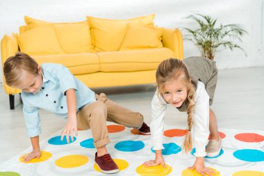 KYIV, UKRAINE - NOVEMBER 21, 2019: cheerful kids playing twister game near yellow sofa