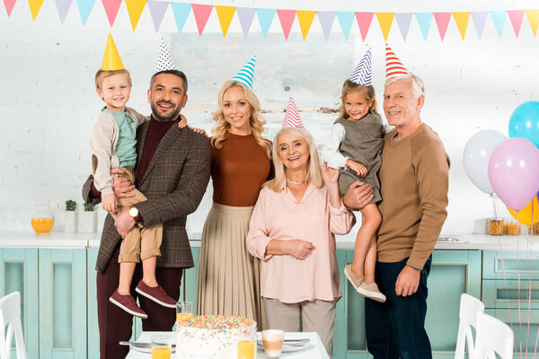 счастливая семья позирует перед камерой, стоя возле торта на кухонном столе
