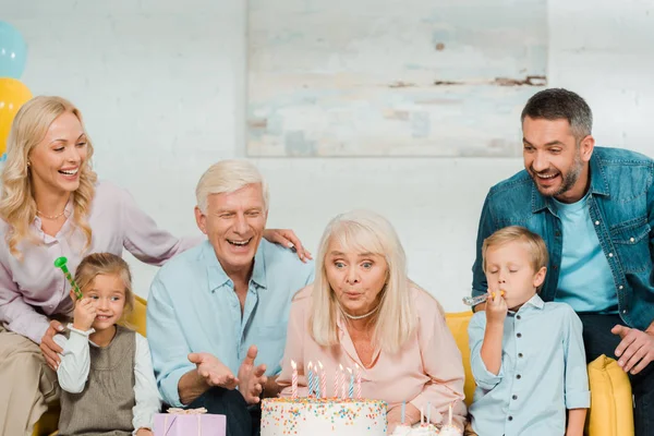 Mulher Sênior Soprando Velas Bolo Aniversário Enquanto Sentado Sofá Perto — Fotografia de Stock