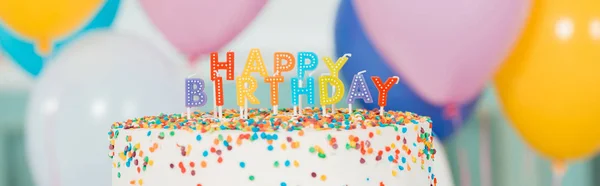 ろうそくのあるおいしい誕生日ケーキとカラフルなお祝いの風船の近くの幸せな誕生日のレタリングのパノラマショット — ストック写真