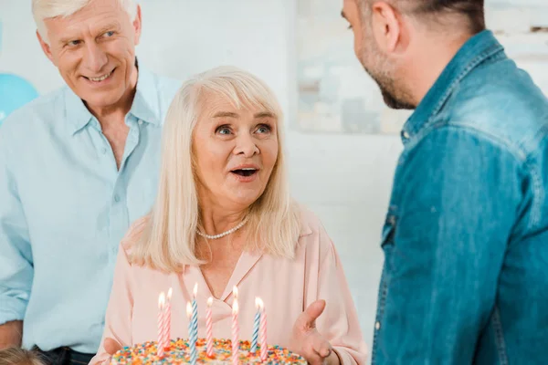 Animado Sênior Mulher Segurando Bolo Aniversário Enquanto Estava Perto Marido — Fotografia de Stock