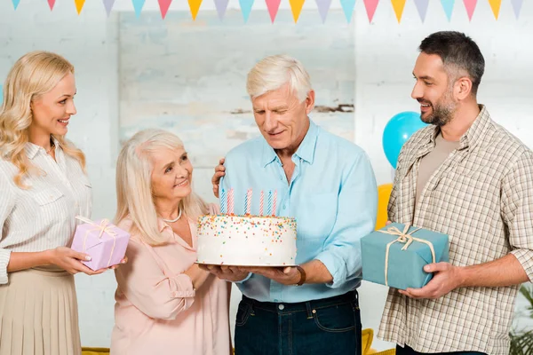 一个快乐的老人站在家人身边 手里拿着生日蛋糕 — 图库照片