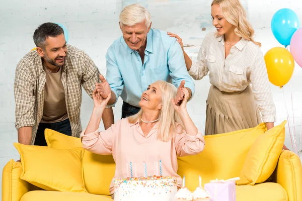 Mulher Sênior Feliz Sentado Sofá Amarelo Perto Bolo Aniversário Família — Fotografia de Stock