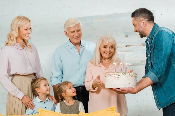 Улыбающийся Мужчина Вручает Торт День Рождения Счастливой Пожилой Женщине Рядом — стоковое фото