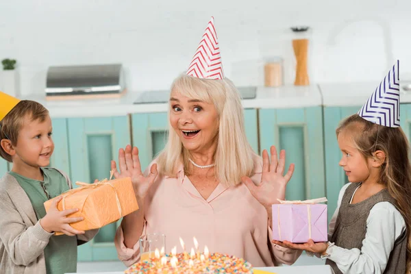 Adorables Nietos Presentando Cajas Regalo Abuela Emocionada Sentada Cerca Pastel — Foto de Stock