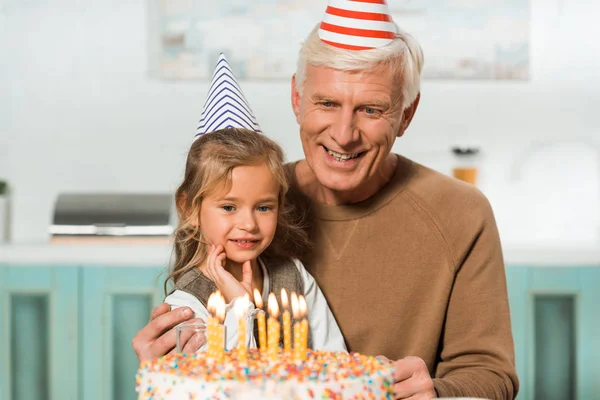 Glad Senior Man Med Bedårande Barnbarn Tittar Födelsedagstårta Med Brinnande — Stockfoto