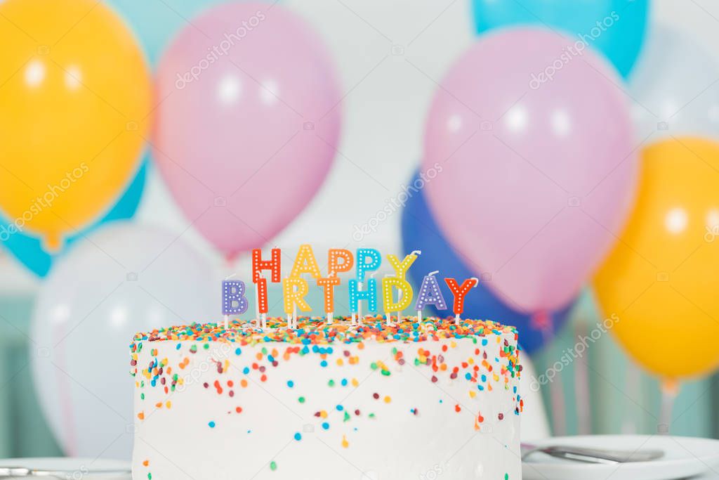 delicious birthday cake with candles and happy birthday lettering near colorful festive balloons