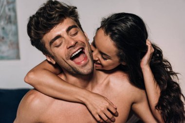 happy woman biting neck of cheerful boyfriend in bedroom clipart