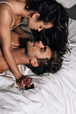 Yatakta erkek üzerinde uzanırken prezervatif tutan seksi kız.